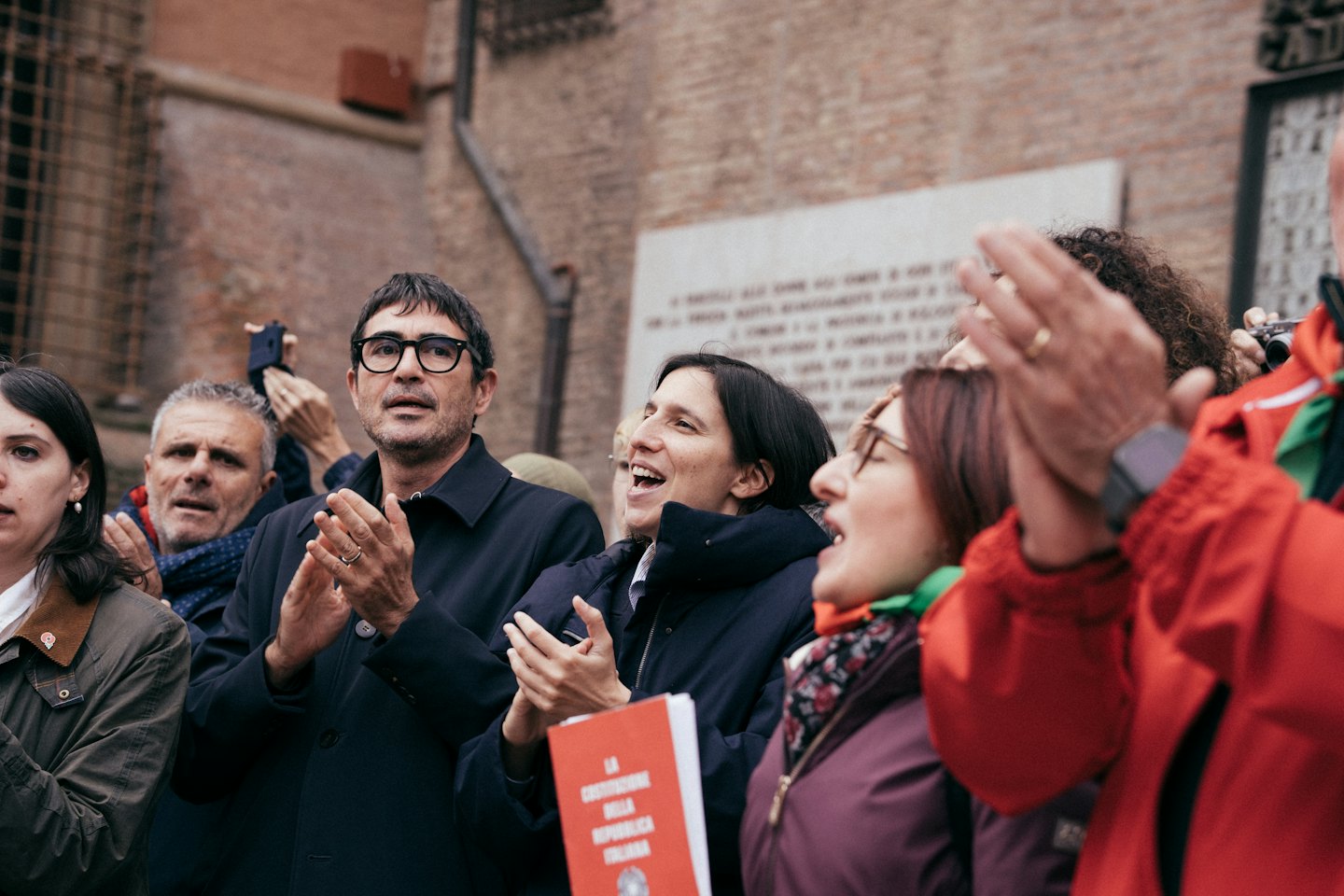 Persone applaudono e fanno il tifo tenendo in mano un libro della costituzione italiana.
