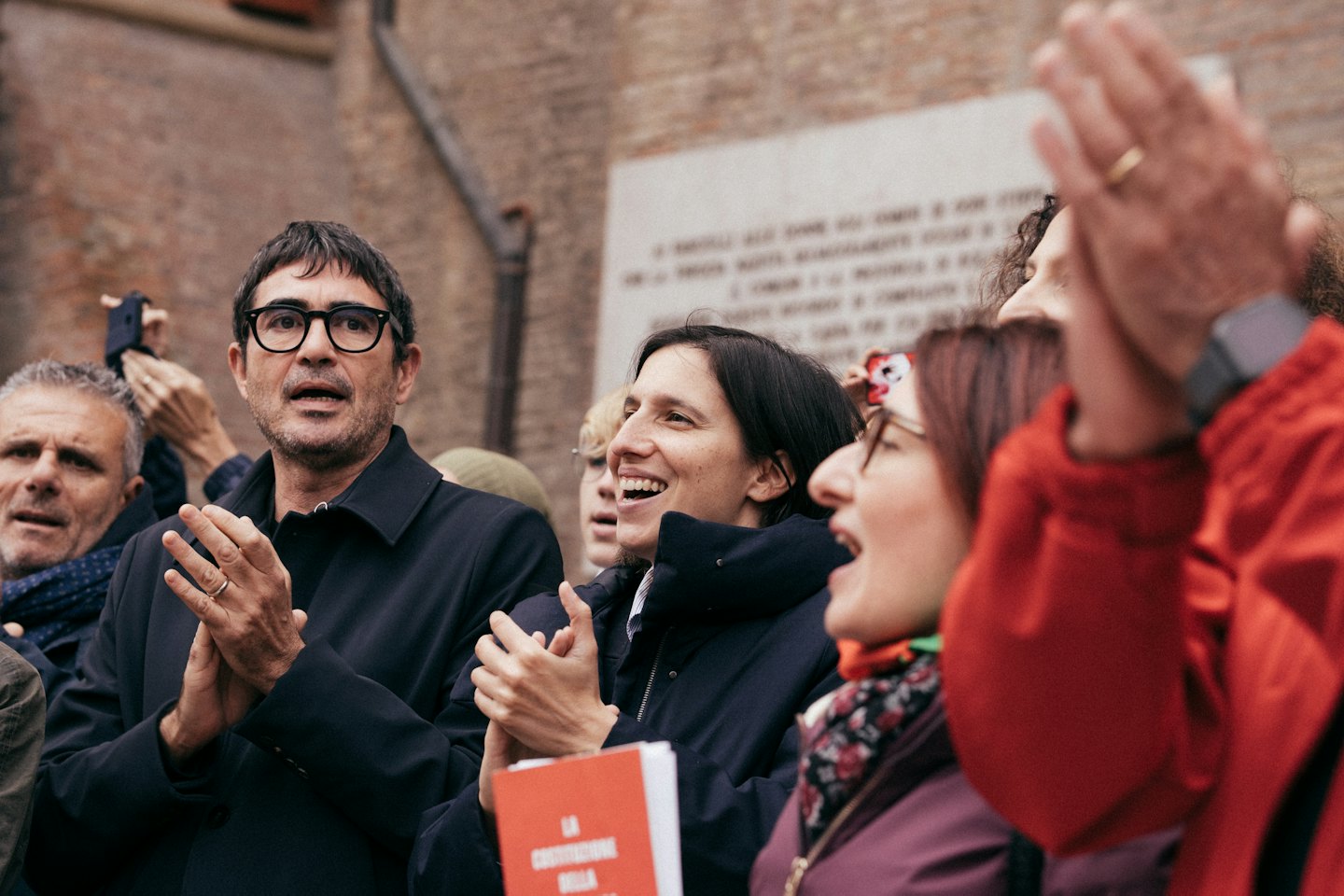 Un gruppo di persone applaude tenendo smartphone a un evento all'aperto.